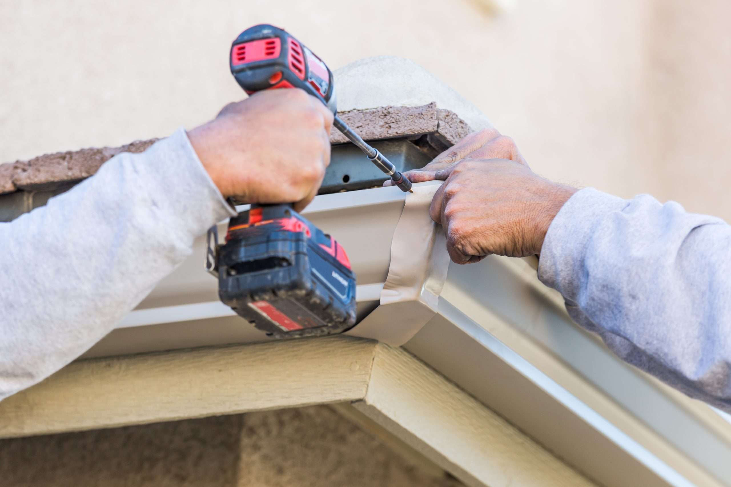 Worker using drill to install gutter on house